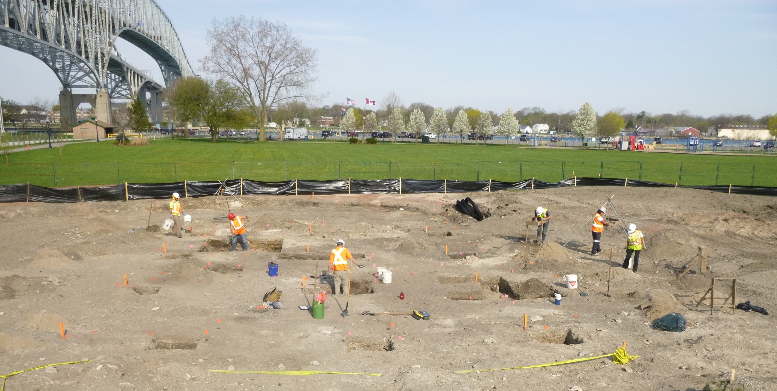An archaeological crew excavates a portion of Waterfront Park in Point Edward. The Blue Water Bridge is visible in the background.