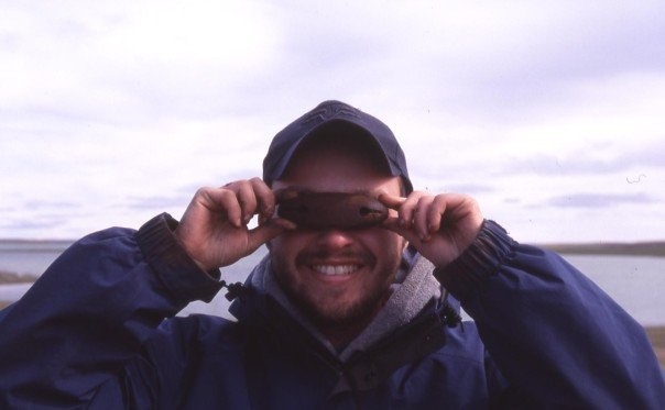 A man in a ball cap and parka demonstrates the use of traditional Inuit Snow Goggles.