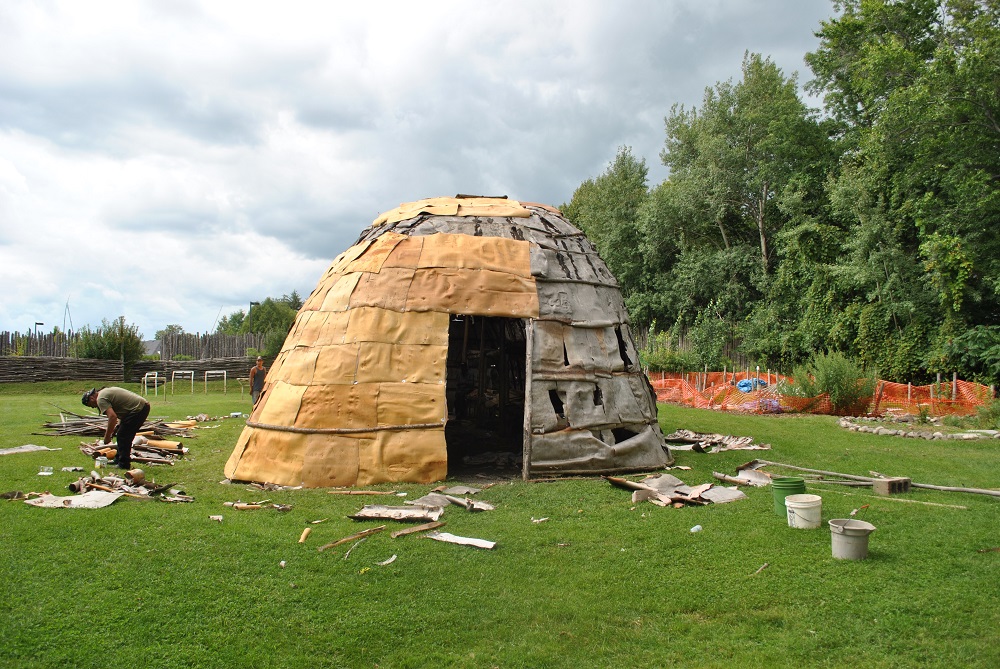 New bark strips are affixed to the large longhouse on the Lawson Site in 2013. The new bark appears yellow next to the old grey bark siding.