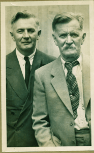 A suited Wilfrid Jury stands next to his father Amos. Both are looking at the camera