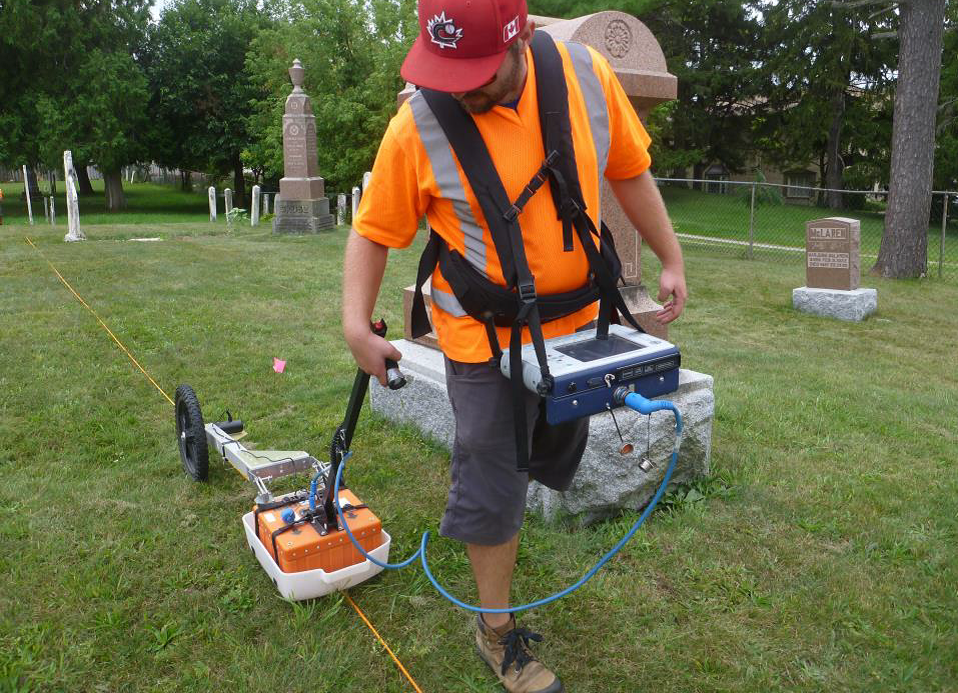 A worker (Tom) pulls the ground penetrating radar unit over a transect in a grassy cemetery.