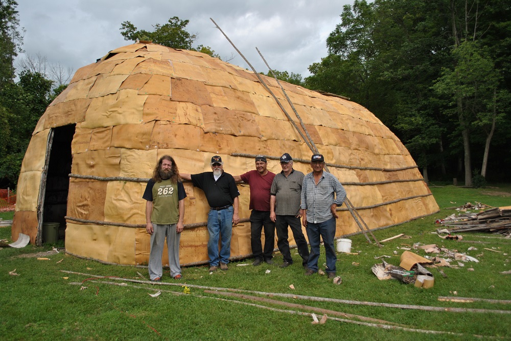 Five crew members stand in front of a completely recovered longhouse on the Lawson Site.