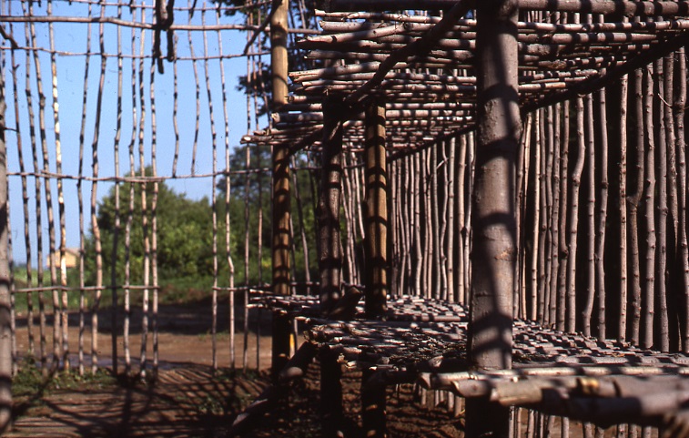 An interior image of the 1980 longhouse reconstruction. Benches appear in the foreground mounted on the primary interior structural poles. The outline of the door is visible in the background