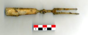 A two-pronged fork artifact, shown fairly intact with a scale bar underneath.