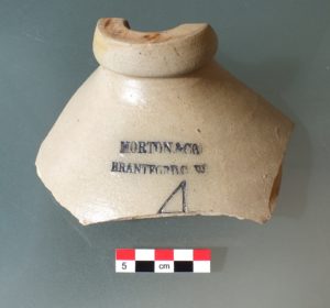 The fragmentary top of a clay bottle artifact. The engraved words "Morton & Co. Brantford C.W." are visible