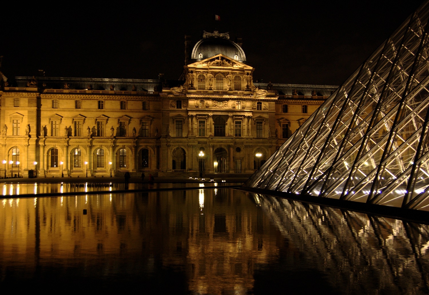 A night image of the illuminated Louvre from the reflecting pool near the front.