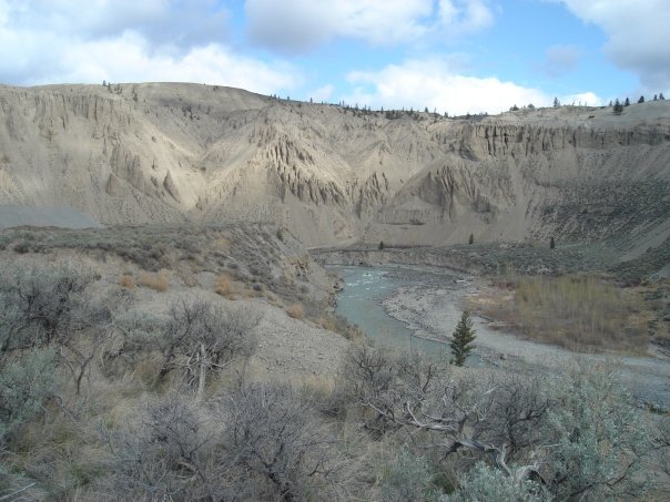 A scenic image of a desert canyon (Farwell Canyon, BC) overlooking a river with sand dunes in the background