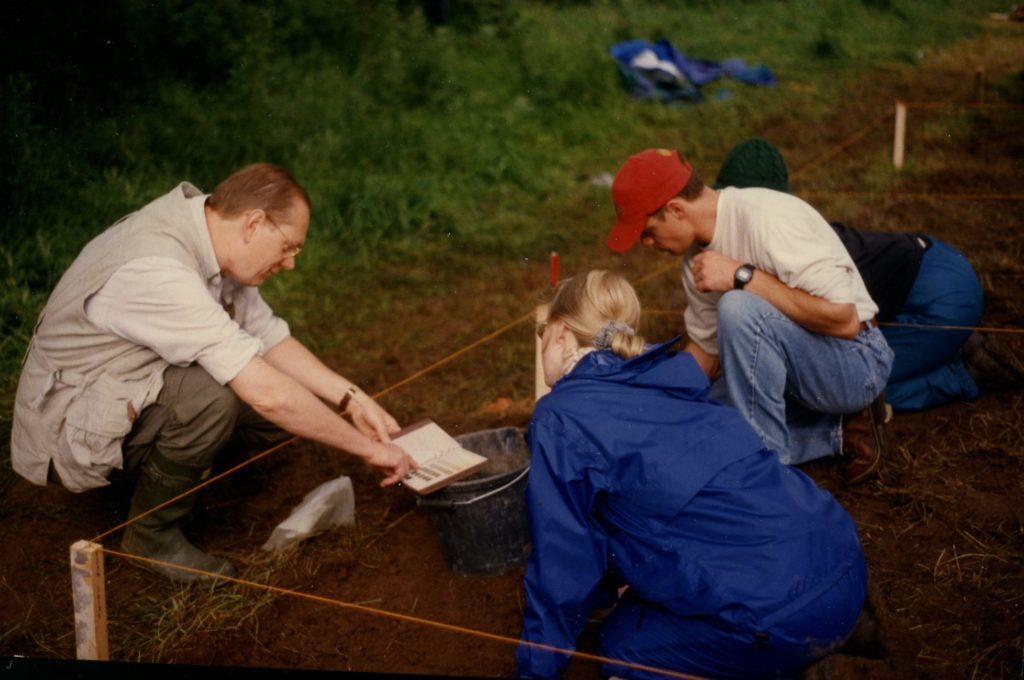 Charles Orser Jr. points to a colour chart on a block excavation with three students looking on.