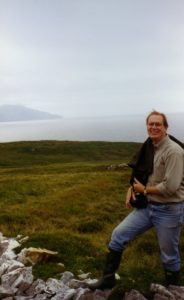 Charles Orser Jr. poses in front of a rolling green slope to a haze-shrouded bay in the background.