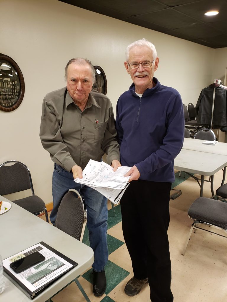 Two volunteers (Chris Ellis and Darryl Dann) pose holding sheets of paper representing the dozens of archaeological sites they've updated for entry in a government database.