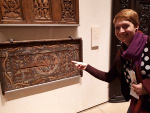 Robyn Lacy points at a wooden artifact mounted on the wall in a museum