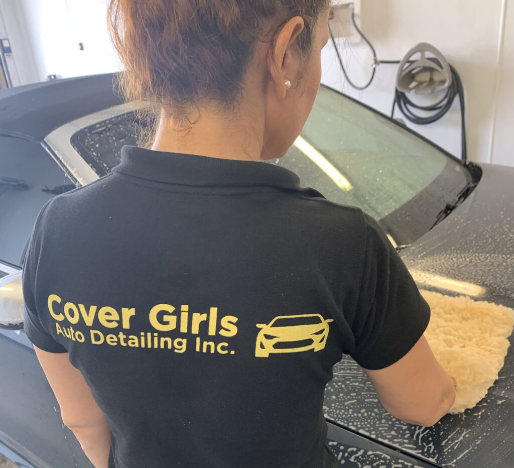 Cover Girls Auto Detailing logo on the black shirt of a women washing a car. 